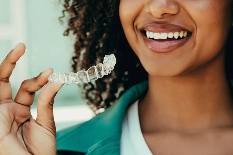 Young adult holding a clear retainer and smiling